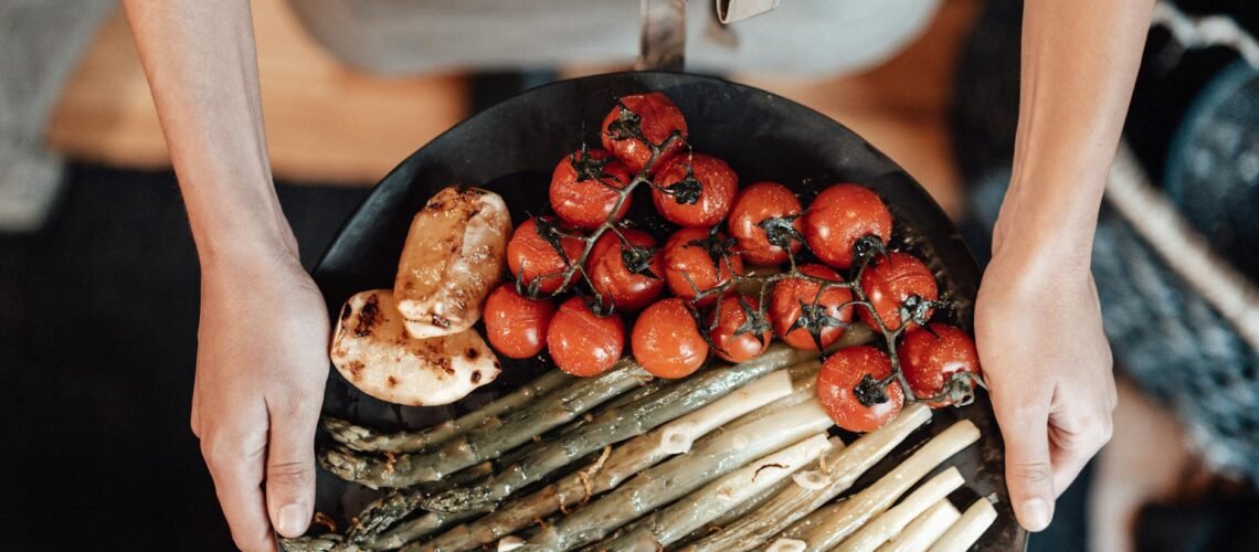 person holding black plate with cherry tomatoes and asparagus